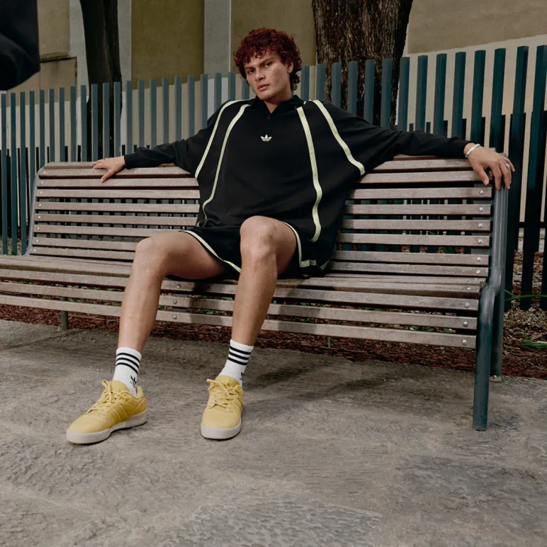 chłopak w ubraniach adidas siedzi na ławce